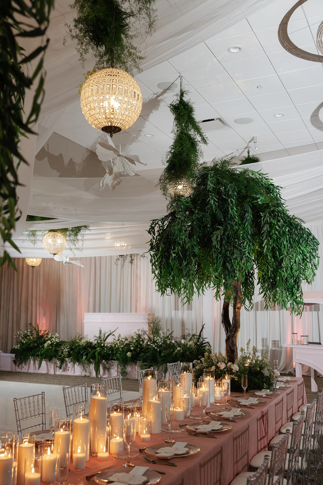 Candlelit reception tables, greenery and chandeliers beside the white dance floor at Waypoint 4180