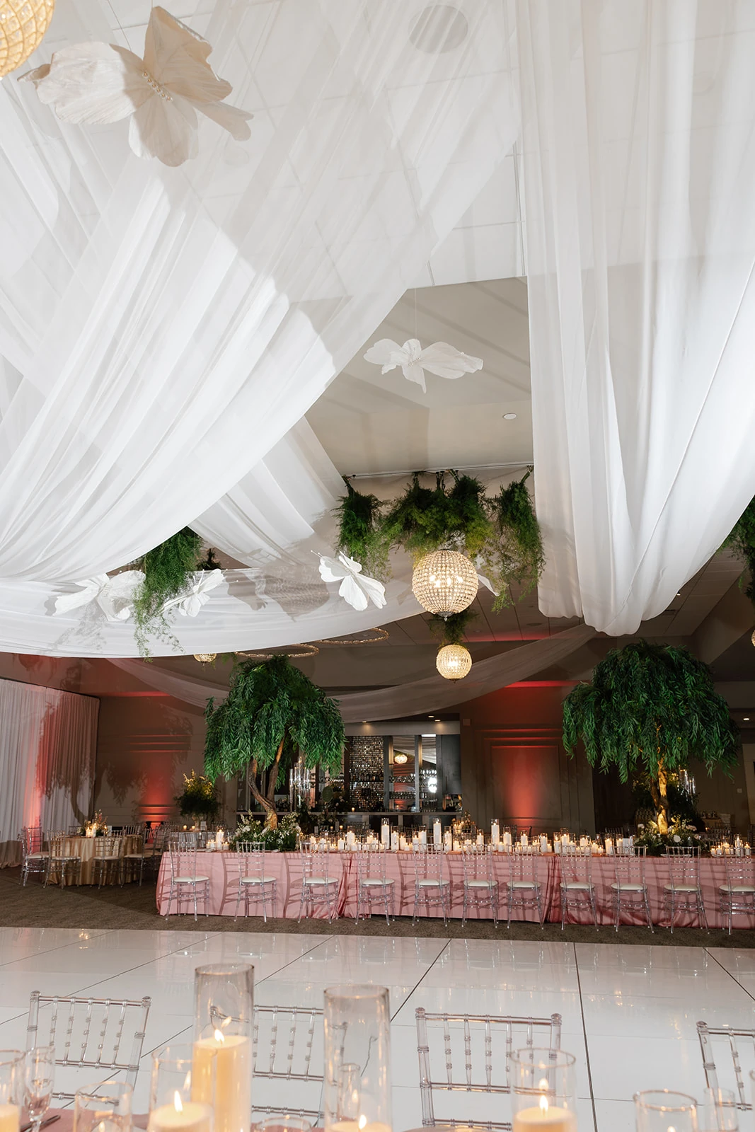 White paneled dance floor in a reception room with ceiling draping, suspended greenery and candlelit tables at Waypoint 4180