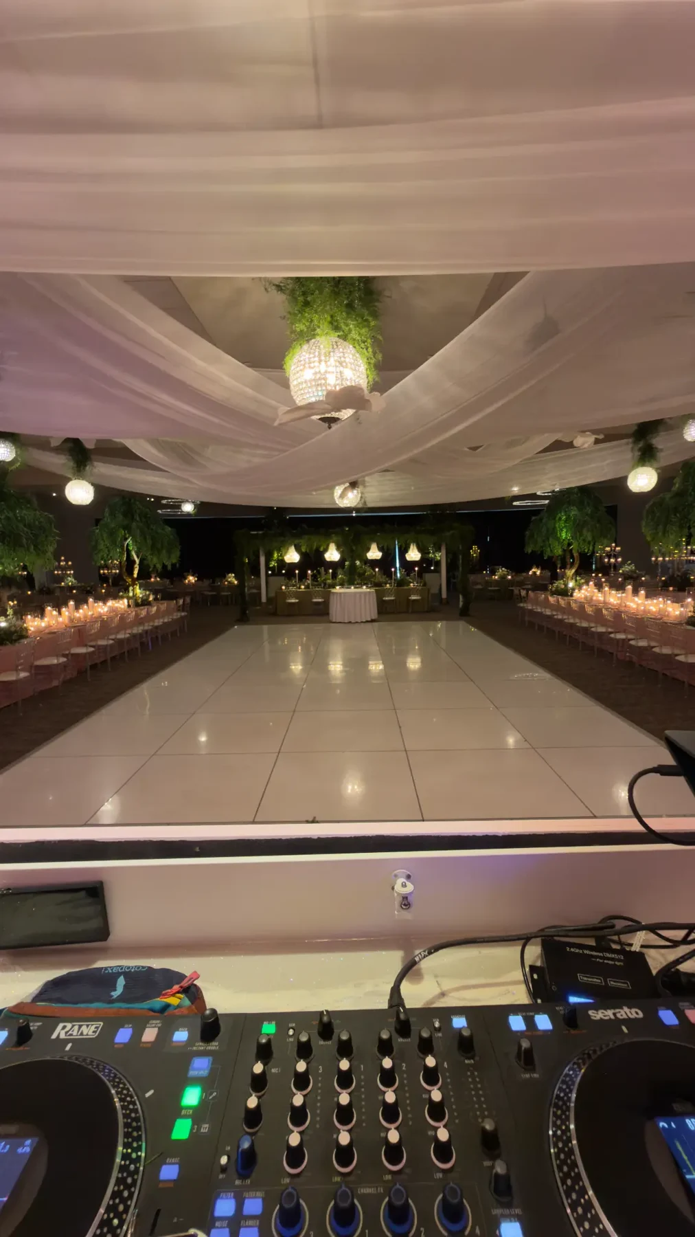 Real all-white dance floor beneath white draping and greenery, seen from behind DJ equipment