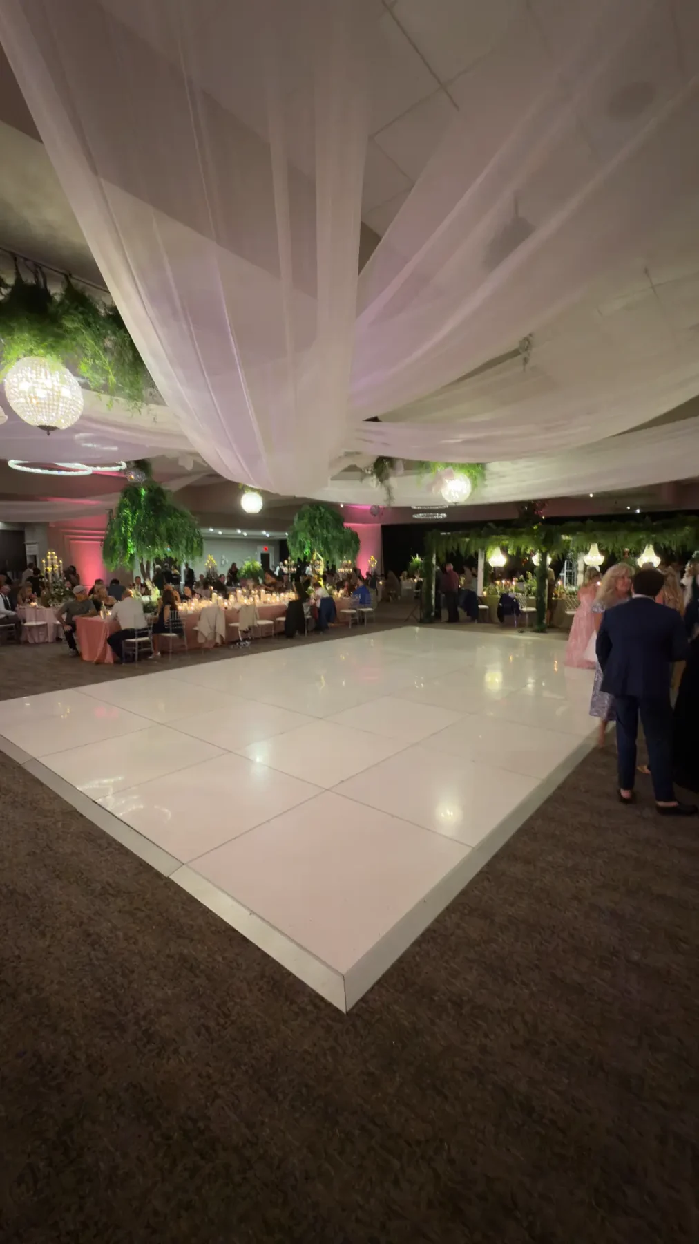 Real glossy white paneled dance floor with an edge ramp beneath fabric draping and chandeliers