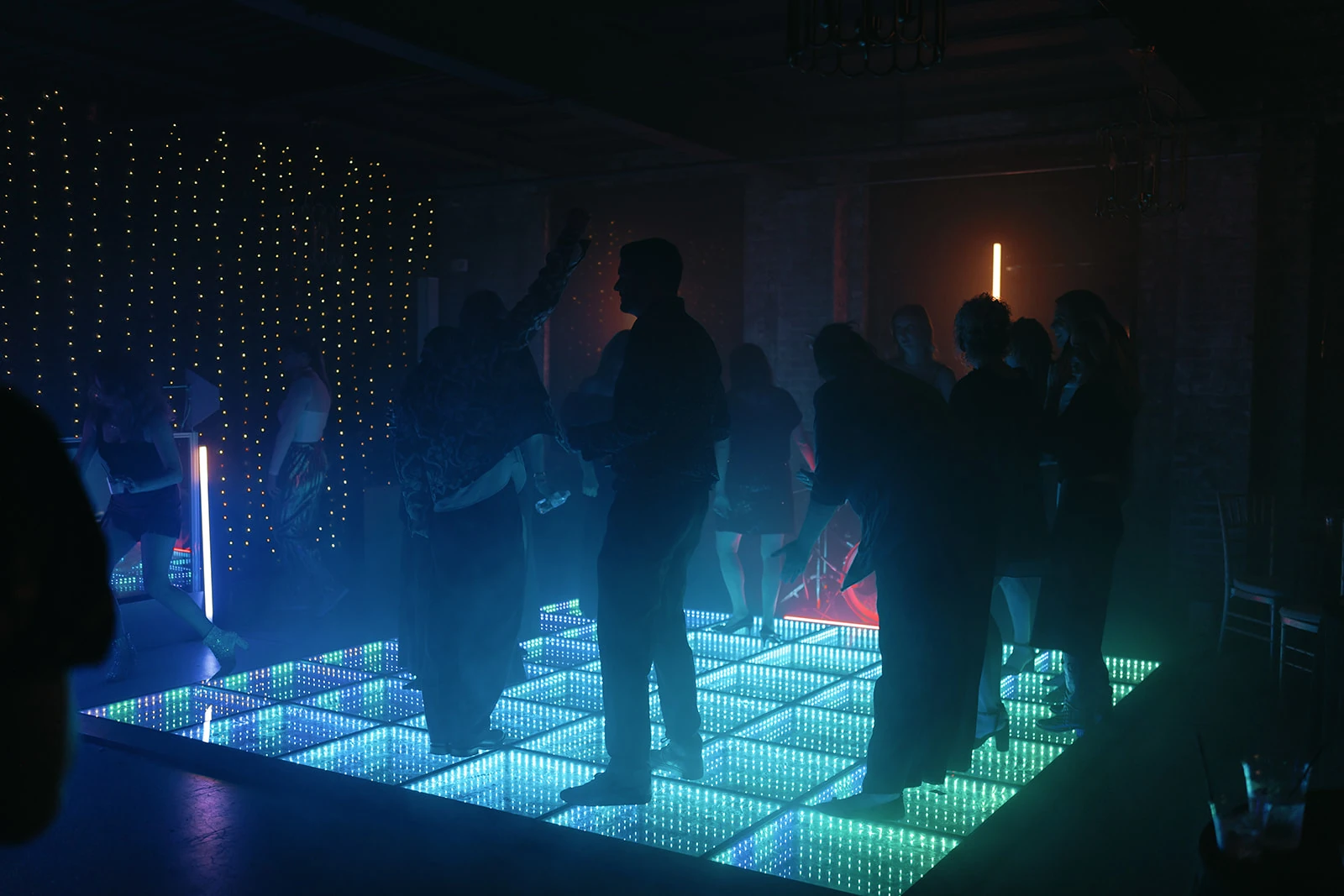 Guests dancing on an illuminated LED floor with blue and green light points in mirrored panels