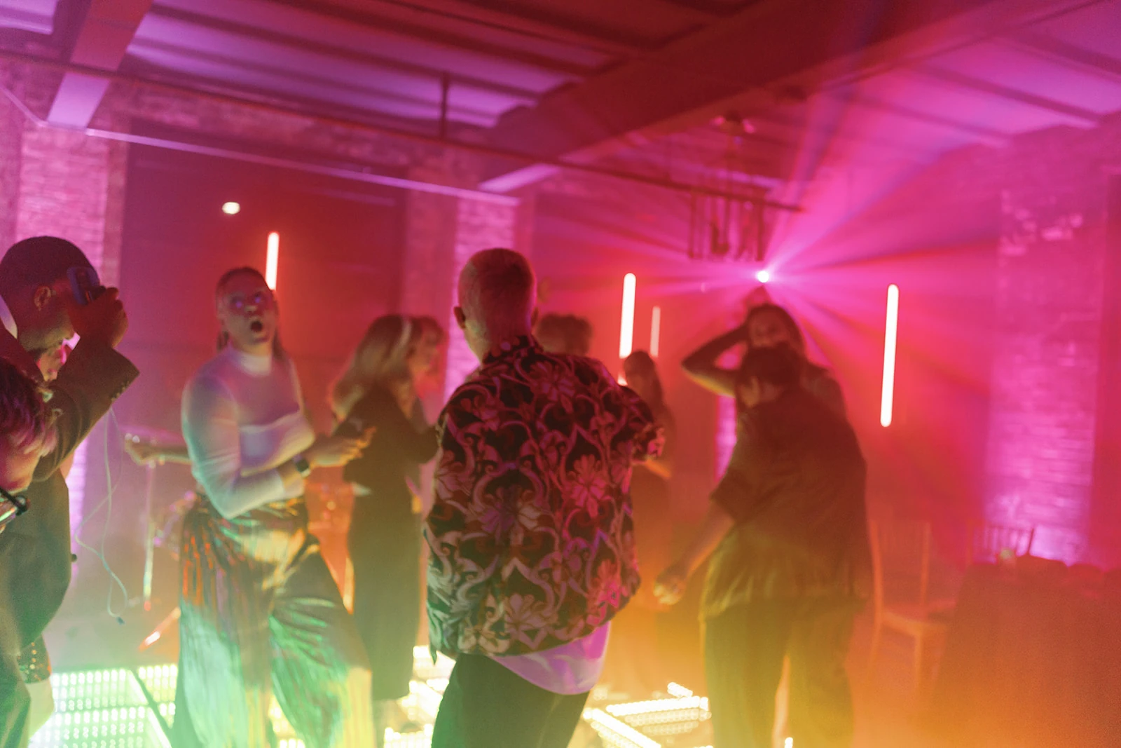 People dancing on a luminous LED floor beneath pink and warm ambient lighting